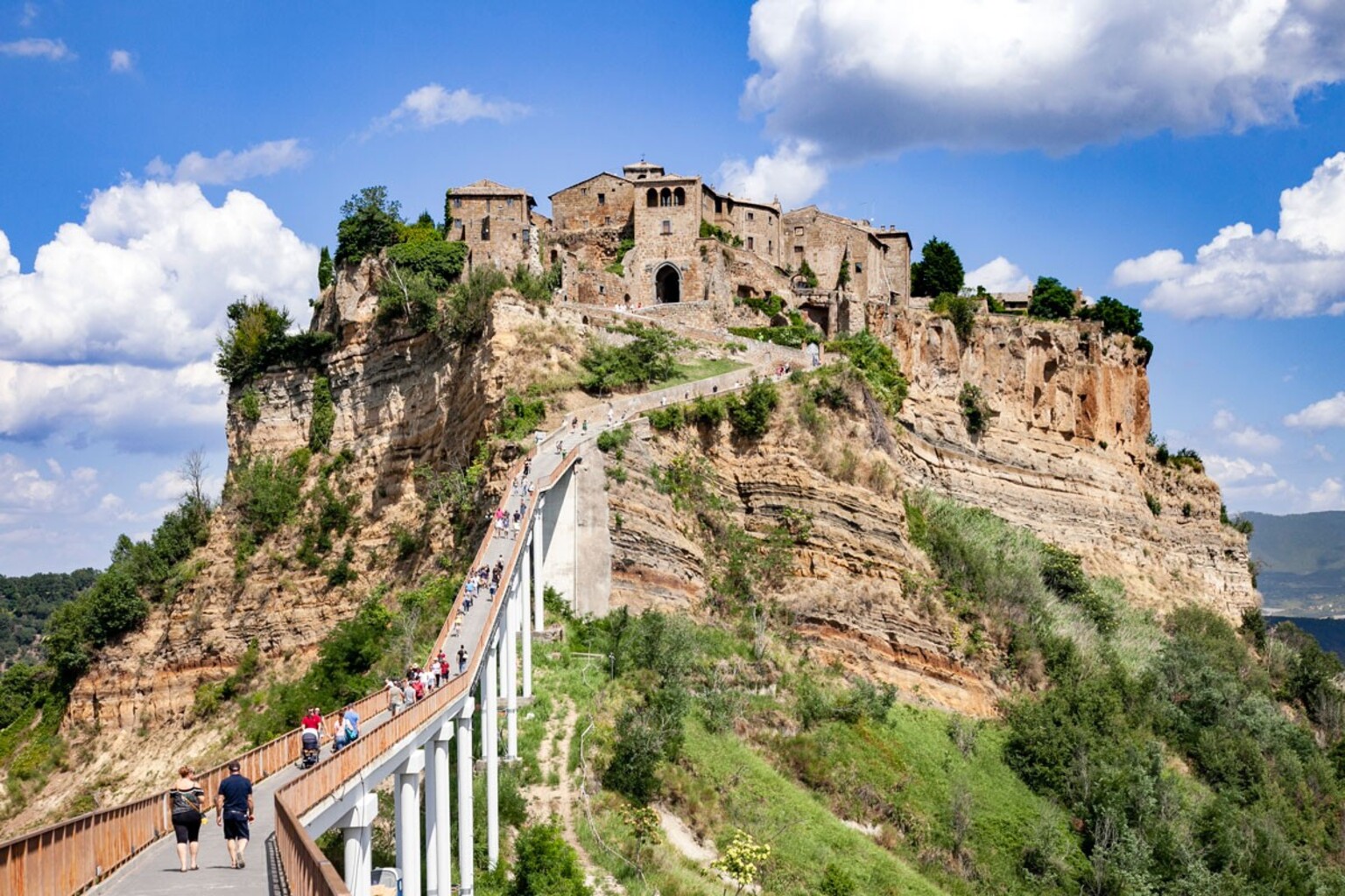 Visitors walking along the pedestrian bridge leading to Civita di Bagnoregio perched on tufa rock cliffs, Umbria Italy