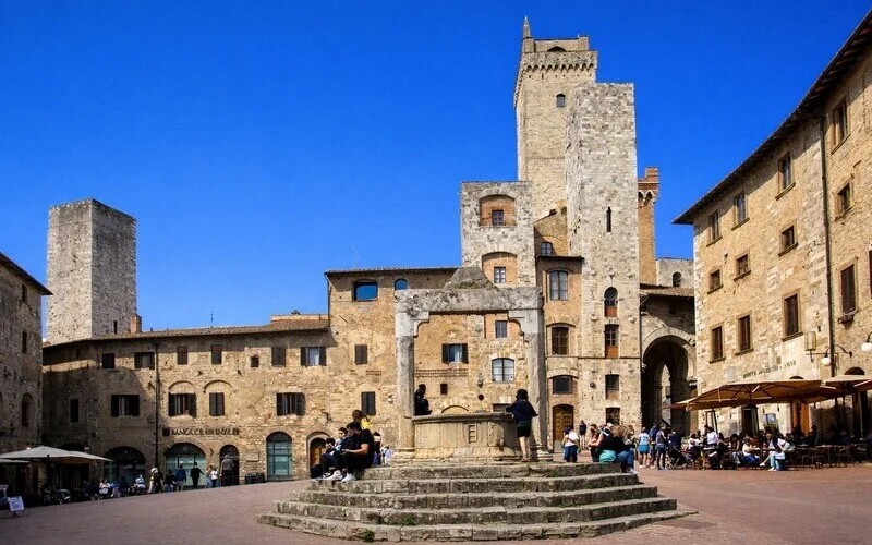 Piazza della Cisterna San Gimignano — herringbone brick square with medieval well and towers, Tuscany Italy