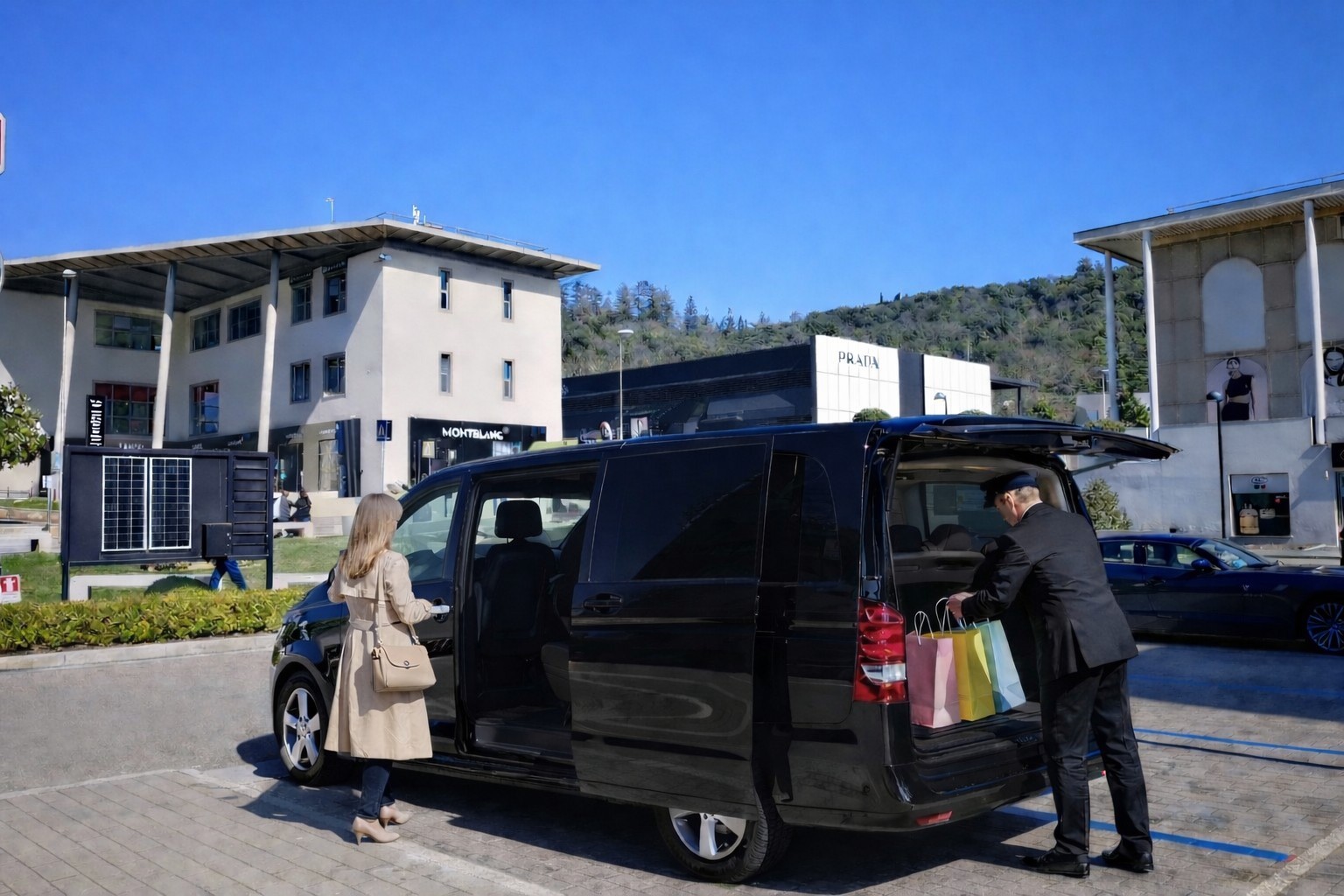 Private chauffeur loading shopping bags into a black Mercedes V-Class at The Mall Firenze luxury outlet with Prada boutique in the background, Tuscany Italy