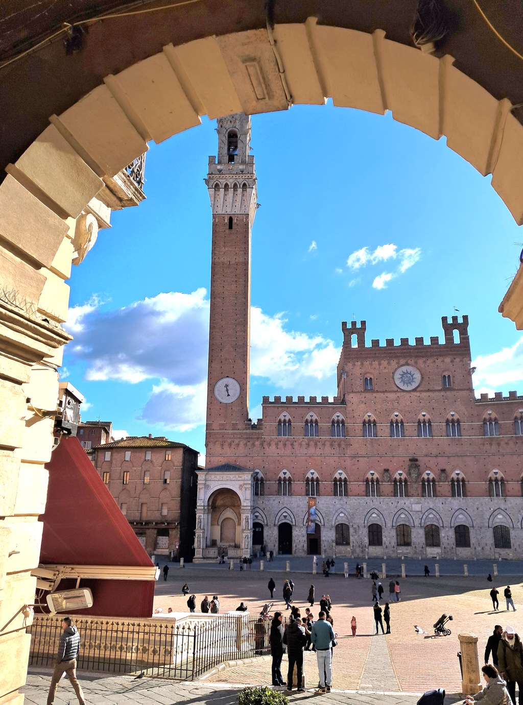 View through a medieval arch of the Torre del Mangia and Palazzo Pubblico in Piazza del Campo, Siena, Tuscany Italy