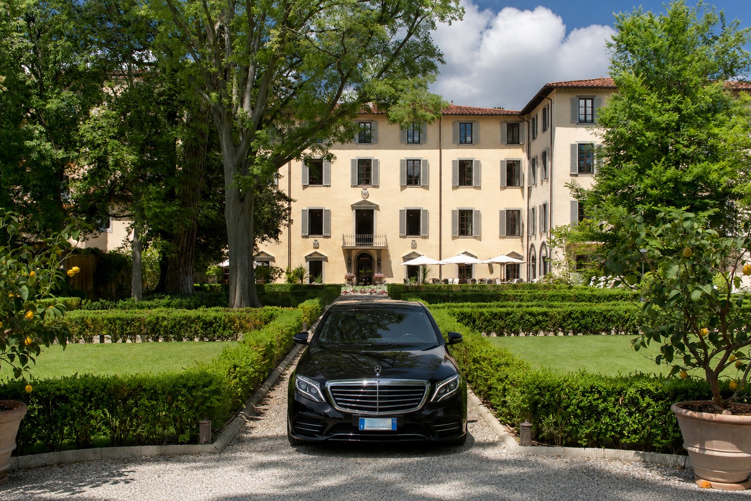 Black Mercedes E-Class parked in the manicured gardens of Four Seasons Hotel Florence, the historic villa visible in the background