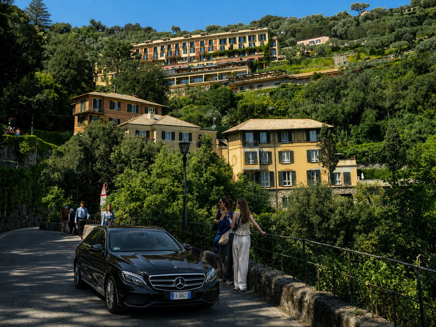Black Mercedes E-Class on the road approaching Hotel Splendido Portofino, the iconic hillside hotel visible above among the Mediterranean greenery