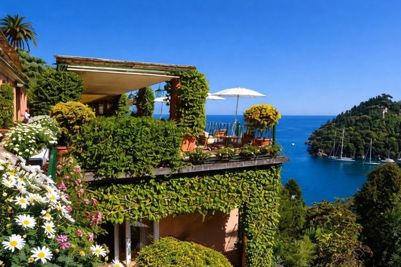 Flower-covered terrace at Hotel Splendido Portofino with white umbrella and view over the Gulf of Tigullio and sailing boats