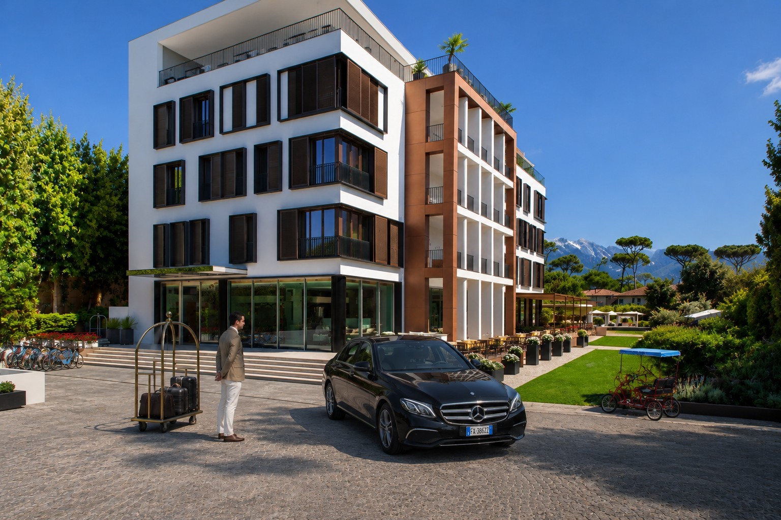 Black Mercedes E-Class arriving at Principe Forte dei Marmi hotel entrance with bellboy and luggage trolley, Apuan Alps in the background