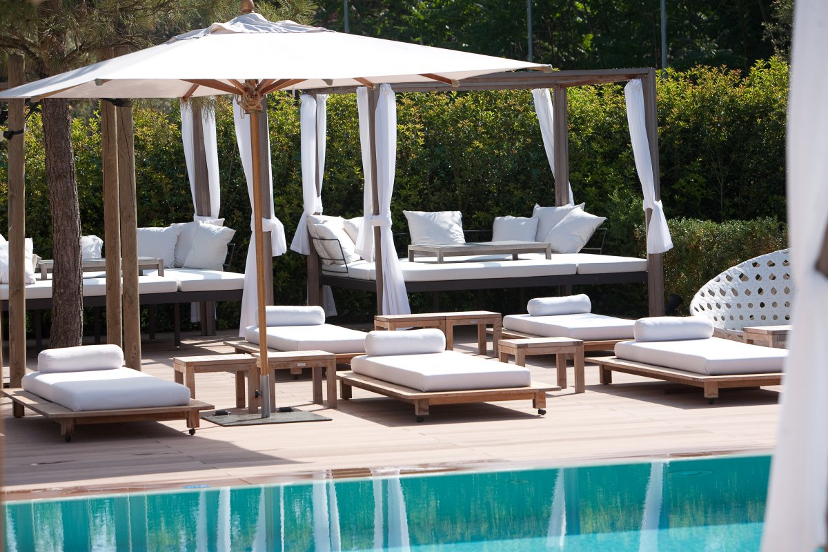 Luxury pool area at Principe Forte dei Marmi with white cushioned sun loungers, cabanas and pine trees